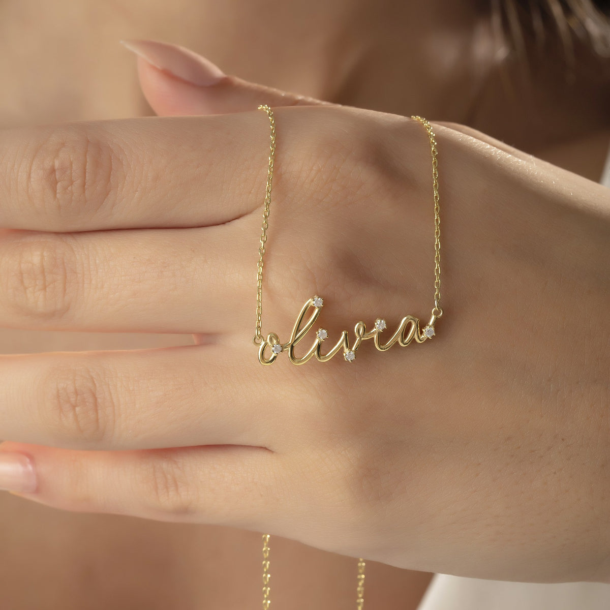 Diamond-look gold name necklace draped over a hand
