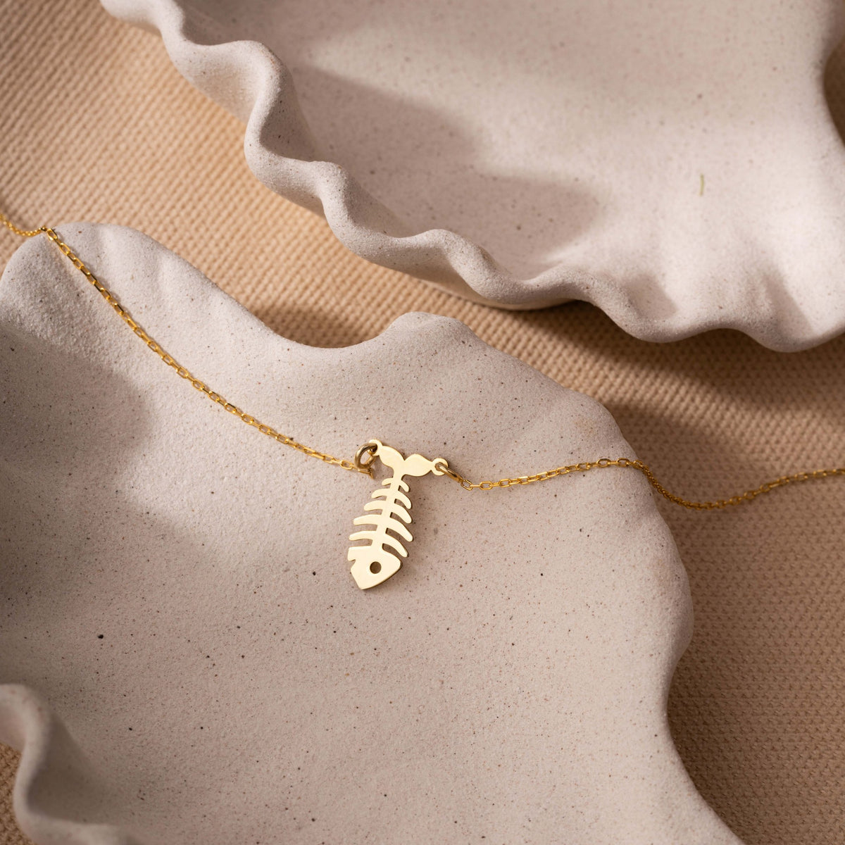 Fish bone pendant close-up in 14K gold vermeil on a ceramic dish