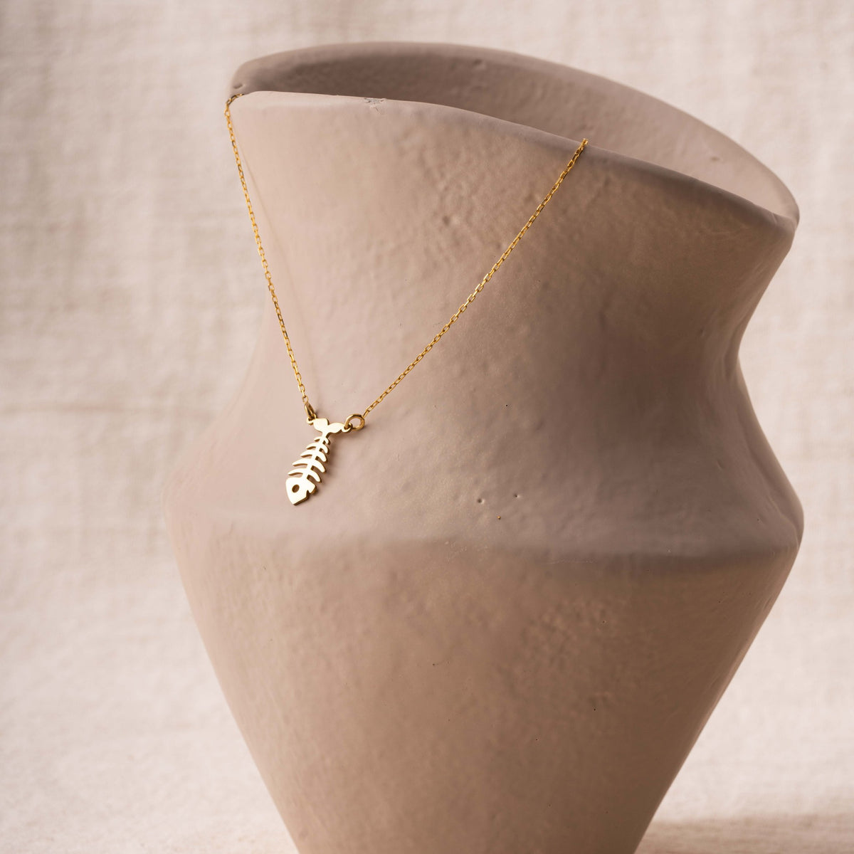 Gold fish skeleton necklace draped on a ceramic vase