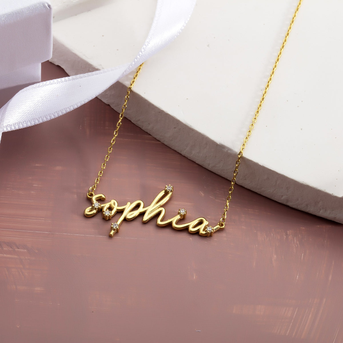 Best friend name necklace gift beside a white gift box and ribbon