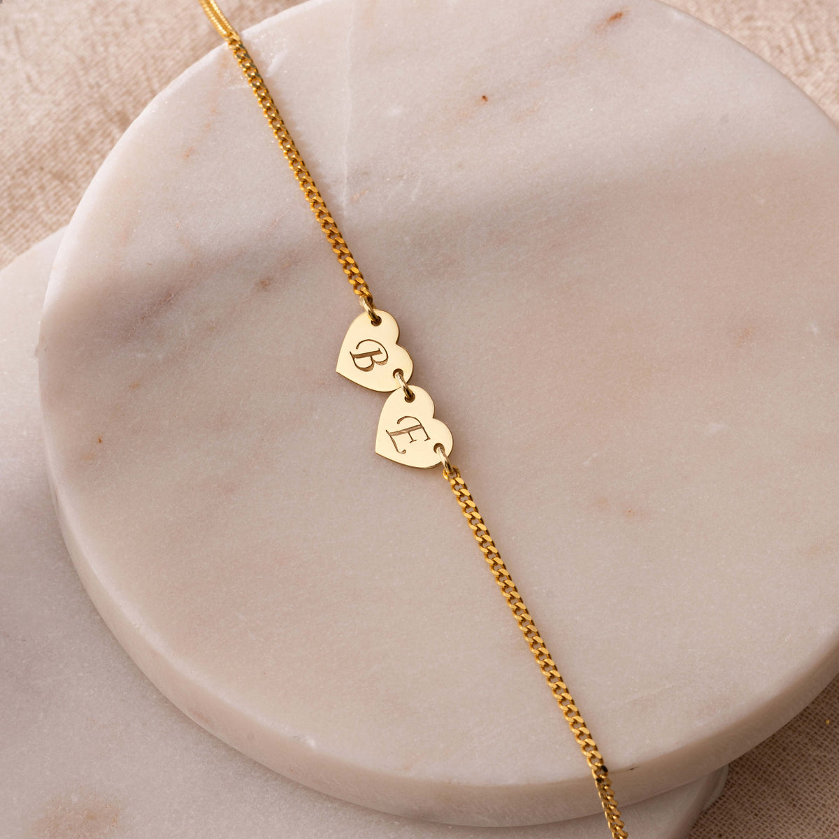 Gold two initial heart necklace on marble, engraved letters B and E