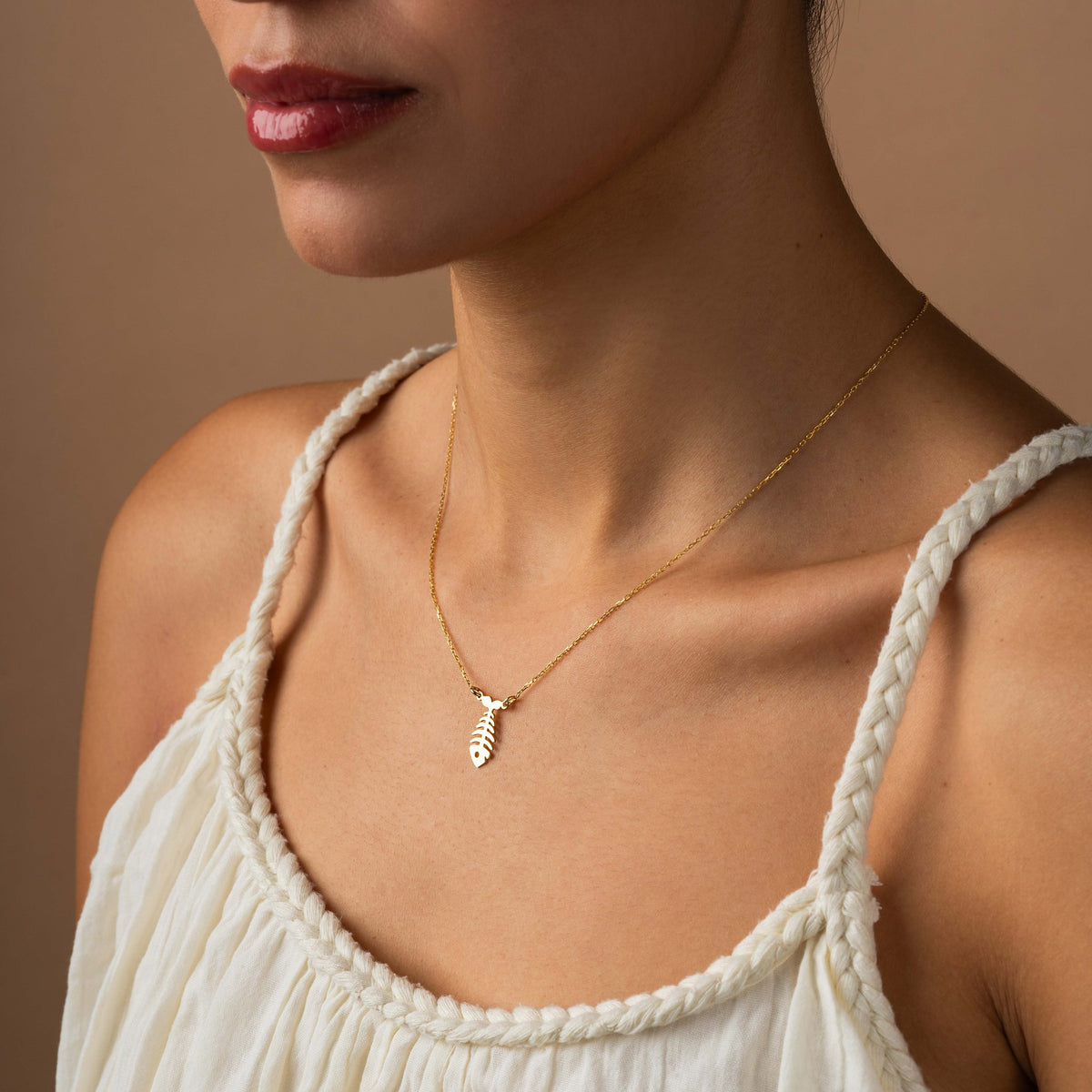Dainty fishbone pendant necklace in 14K gold vermeil worn by a woman