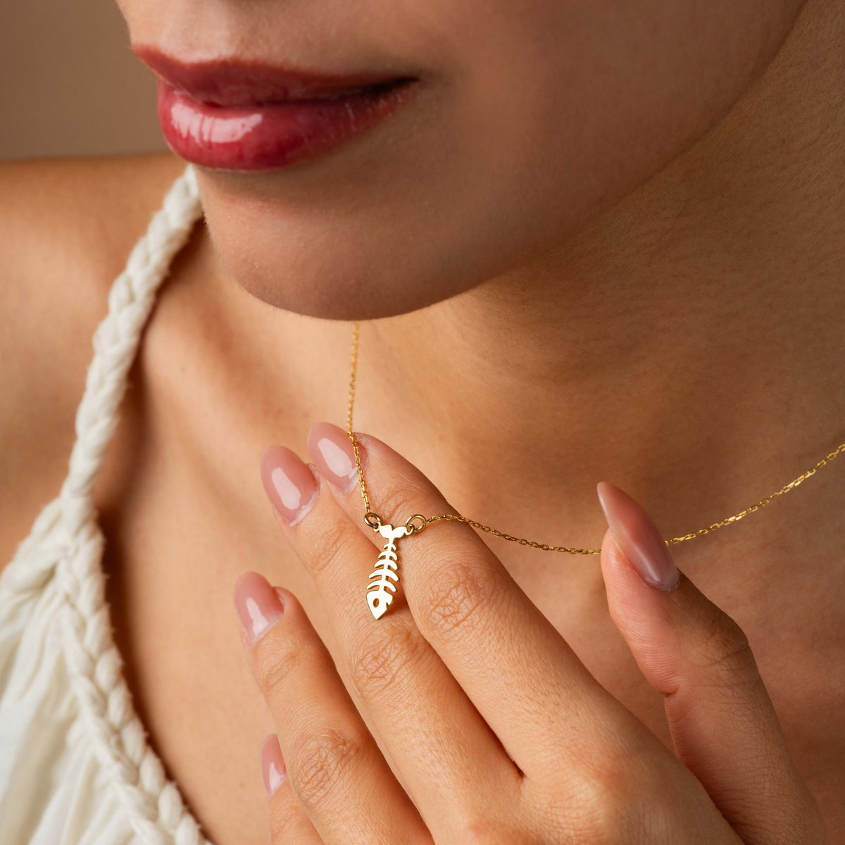 Fishbone charm necklace held between fingers at the collarbone