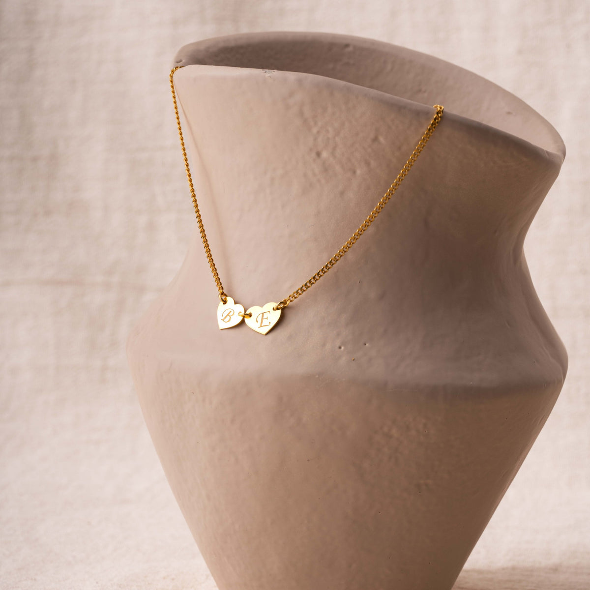 Dainty gold initial heart necklace displayed on a ceramic vase